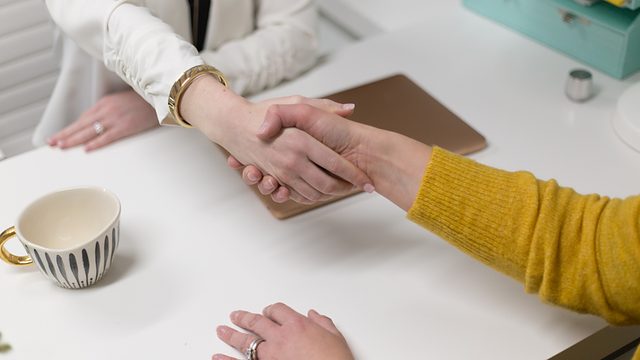 Two people shaking hands across a desk