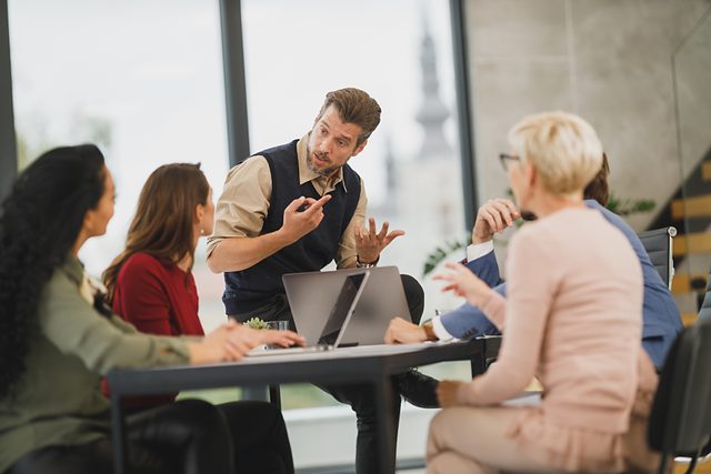 Presenter speaking to colleagues seated around a meeting table